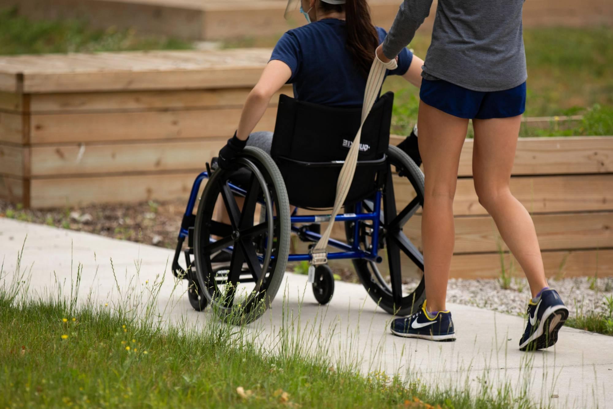 Person pushing another person in wheelchair on sidewalk